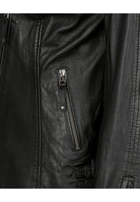 Schwarze Lederjacke mit einer Reißverschlusstasche an der Seite, strukturiertem Oberflächenfinish und Steppnähten entlang der Kanten und Nähte.
