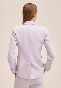 Fioletowa marynarka o dopasowanym kroju, z wyciętymi klapami i subtelnym wypełnieniem ramion. Posiada rozcięcie z tyłu oraz mankiety zapinane na guziki.