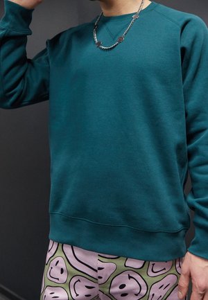 Teal sweatshirt met ronde halslijn en geribde manchetten, gecombineerd met een korte broek met een patroon van groene en roze abstracte ontwerpen.