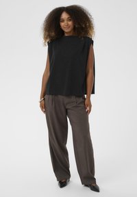 Mustra musta ilma varrukateta topp, millele on sobitatud laiad pruuni värvi püksid, millel on ees voldid ja kitsenev lõige, ning täiendavad terava nina mustad kingad.