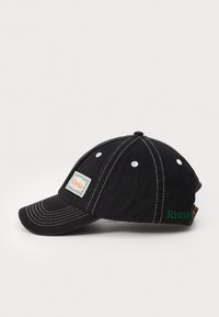 Casquette en coton noir avec une visière courbée, des coutures blanches et une broderie sur le côté en vert. Présente une étiquette rectangulaire à l'avant. Tissu texturé.