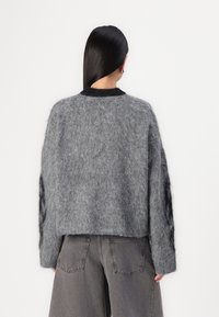 Grijze, fluffy cropped sweater met lange mouwen en een zwarte ribgebreide kraag, gecombineerd met high-waisted donkergrijze jeans.