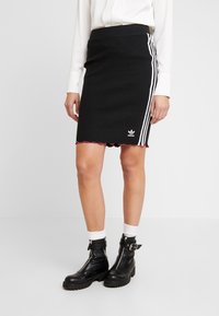 Svart ribbad kjol med vita sidskarvar och scallopad nederkant. Adidas-logotyp på nedre framsidan. Matchad med svarta kängor och vita strumpor.