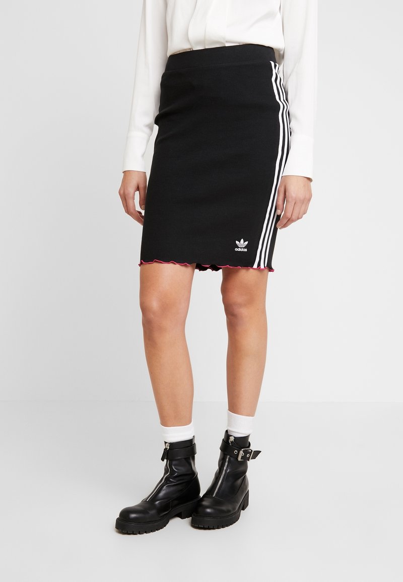 Svart ribbad kjol med vita sidskarvar och scallopad nederkant. Adidas-logotyp på nedre framsidan. Matchad med svarta kängor och vita strumpor.