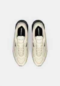 Ζευγάρι κρεμ Nike Air Max παπούτσια με μαύρες λεπτομέρειες, σε προοπτική πάνω από μια λευκή φόντο.