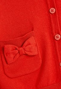 Cardigan rosso a maglia con tasca decorata da un fiocco e bottoni coordinati lungo la parte anteriore. Texture liscia e design a maglia stretta.