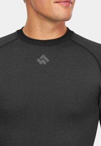 Czarna sportowa bluzka z długim rękawem o teksturowanej tkaninie, z okrągłym dekoltem i subtelnym logo na środku klatki piersiowej.