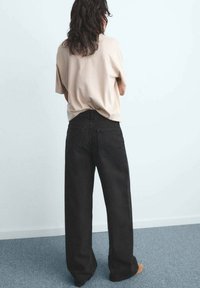 Relaxed-fit beige t-shirt met opgerolde mouwen, gecombineerd met zwarte jeans met hoge taille en brede pijpen. Zachte stof, gladde structuur, minimale stikdetails.