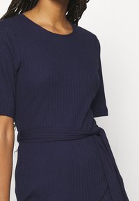 Navy-blaues Rippenkleid mit kurzen Ärmeln, das über einen runden Ausschnitt und einen gebundenen Gürtel in der Taille verfügt. Glatte Textur mit vertikalen Linien.