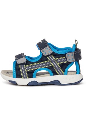 Las sandalias para niños cuentan con una parte superior de malla en color azul marino con acentos en azul, costuras amarillas, correas ajustables y una suela blanca acolchada con una parte inferior texturizada.