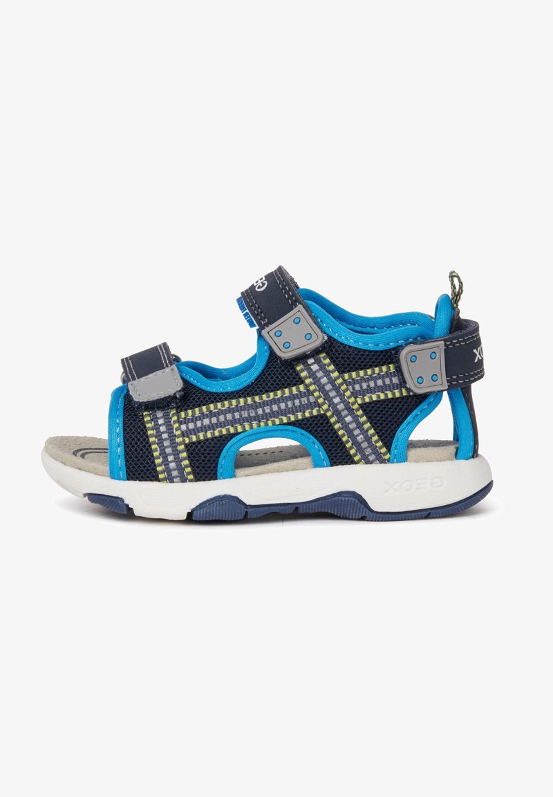 Las sandalias para niños cuentan con una parte superior de malla en color azul marino con acentos en azul, costuras amarillas, correas ajustables y una suela blanca acolchada con una parte inferior texturizada.
