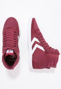 Zapatillas altas de tela y ante burdeos, con un diseño de chevrón blanco, cordones redondos y suela de goma. Se aprecia un sutil acento con el logotipo.