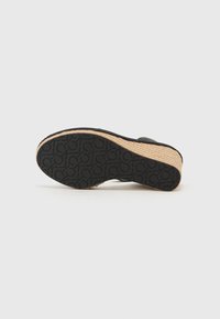 Espadrille sole with a woven jute base, black rubber outsole featuring a patterned grip, and curved shape for slip-on design.