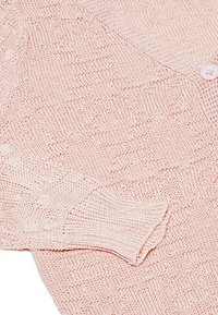 Cardigan lavorato a maglia rosa chiaro con un motivo testurizzato, chiusura con bottoni e polsini a coste. Il materiale sembra morbido e traspirante.