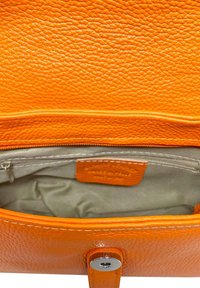 Interior de un bolso de mano de cuero naranja que muestra una superficie texturizada, un compartimento con cremallera y un forro suave con una pequeña etiqueta.