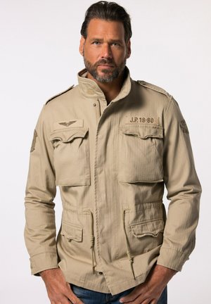 Beige Militärjacke im Stil mit hohem Kragen, zwei Brusttaschen und verstellbaren Zugbändern in der Taille. Strukturierter Stoff mit Schulterklappen.