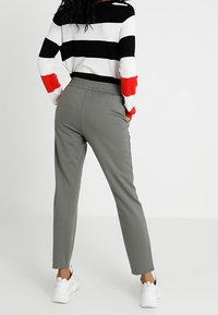 Grijze elastische taillebroek met een taps toelopend been, gecombineerd met een gestreepte trui in zwart, wit en rood. De stof lijkt soepel en casual.