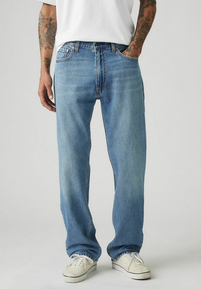 Jeans de mezclilla de color azul claro con un corte relajado, diseño de cinco bolsillos y un ligero desvanecimiento. Combinados con zapatillas blancas.