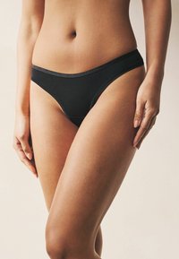 Tanga in cotone nero con finitura liscia, dotato di una ampia cintura elastica con dettagli sottili, design attillato e vita media.