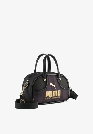 Schwarze und dunkelviolette Puma-Handtasche mit zwei Griffen, abnehmbarem Schulterriemen, goldfarbenem Logo und dem Schriftzug "MACHT'S MIT QUALITÄT" auf der Vorderseite.