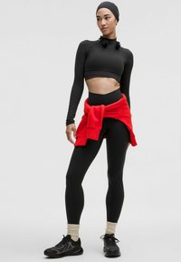 Sort langærmet crop top, sorte leggings, rød sweatshirt bundet om livet, beige sokker og sorte sneakers med teksturerede accenter.