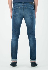 Vaqueros de mezclilla azul oscuro con un corte ajustado, que presentan bolsillos traseros, detalles de costura sutiles y dobladillos doblados a la altura de los tobillos. Llevados con zapatos negros.