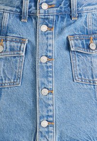 Gros plan sur un tissu en denim bleu avec des boutons en métal et deux rabats de poche avec des coutures orange sur le devant d'un vêtement.