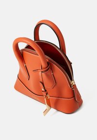 Petit sac à main en cuir orange avec une forme structurée, deux poignées arrondies et des accents en métal doré. Il dispose d'une fermeture éclair et de coutures contrastantes.