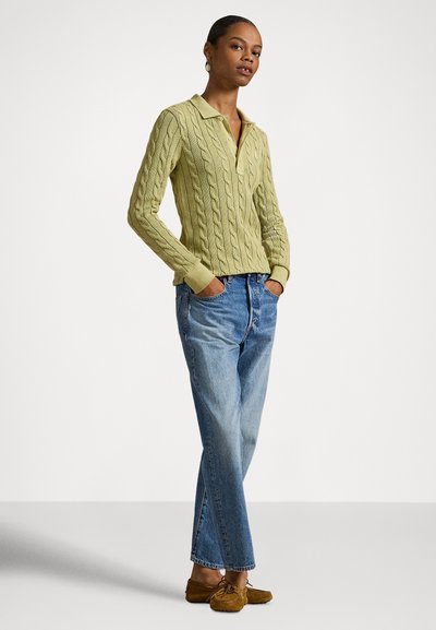 Svetlo zelena pulover iz pletene preje z ovratnikom, kombiniran z modrimi kavbojkami s pravimi hlačnicami in rjavimi čevlji v stilu mokasin. Preprost dizajn in tekstura.