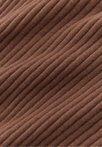 Zbliżenie na miękką brązową dzianinę o prążkowanej fakturze z ukośnymi, wypukłymi liniami tekstury.