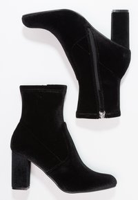 Bottines en velours noir avec tige ajustée, détail de fermeture éclair latérale et talons carrés, présentant une texture lisse et un design élégant.