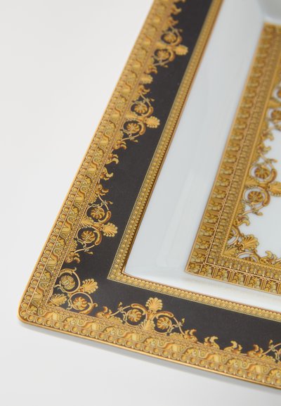 Taisnstūrveida šķīvis ar baltu keramikas centru, zelta un melnas krāsas grezns apmale ar ziedu un arhitektūras rakstiem. Malas ir akcentētas ar zeltu.