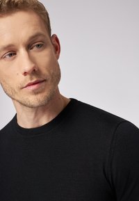Maglione nero a girocollo con una texture liscia, design aderente e maniche corte, che mostra una vista ravvicinata del colletto e della spalla.