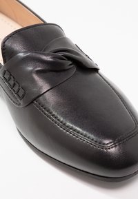 Mocassin en cuir noir avec un bout carré arrondi et une lanière en cuir torsadée sur le dessus.