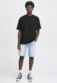 Cămașă simplă din bumbac negru cu un buzunar pe piept, asortată cu pantaloni scurți din denim albastru deschis și adidași negri cu talpă albă.
