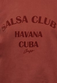 Tissu rouge avec texte rouge foncé disant « SALSA CLUB » en arc au-dessus de « HAVANA » et « CUBA », avec une petite signature « Boss » en dessous.