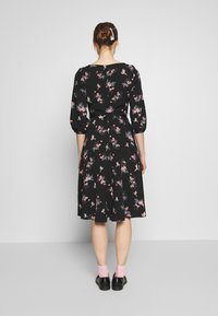 Svart blommig klänning med puffärmar i trekvarts längd, markerad midja och utsvängd kjol. Rosa strumpor och svarta skor fulländar outfiten.