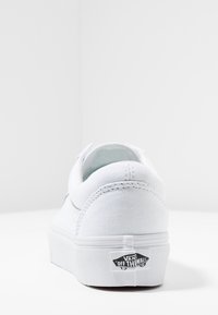 Baskets en toile blanche avec un talon arrondi, un rembourrage et une semelle extérieure texturée. Présente un logo noir "Off The Wall" sur le talon.