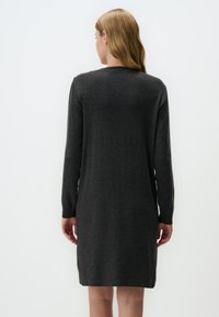 Robe en tricot gris charbon avec des manches longues, un col rond et une coupe droite. Texture douce, longueur genou, minimalisme dans les détails.