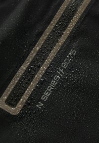 Tissu waterproof noir avec des gouttes d'eau, présentant une bande beige et un texte en relief indiquant "N SERIES // 2015." Texture lisse.