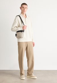 Helle beige Sweatshirt mit Kragen, beige Hose und cremefarbenen Sneakers. Eine kleine Umhängetasche in Grau mit einem schwarzen Riemen. Minimalistisches Design.