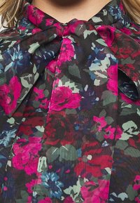 Camicia floreale con sfondo nero, decorata con grandi fiori rosa, rossi e blu. Tessuto morbido con colletto a cravatta e chiusura a bottone.