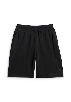 Chłopiec stoi z rękami w kieszeniach, ubrany w szarą koszulkę z napisem "95 racing", czarne krótkie spodenki, białe skarpetki i czarno-białe trampki.