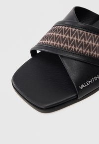 Czarna klapka na ślizgu z szerokim materiałowym paskiem o geometrycznym wzorze w odcieniach różu, połączona z gładką, fakturowaną wkładką.