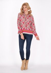 Blomstermønstret bluse i pink og hvid med en bundet halsudskæring, parret med mørkeblå jeans og beige cowboystøvler.