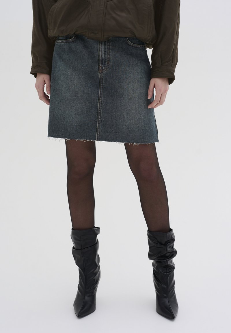 Jeanskjol med trasig nederkant, mörkblå färg, två framfickor, kombinerad med svarta knähöga, avslappnade läderstövlar och genomskinliga svarta strumpbyxor.