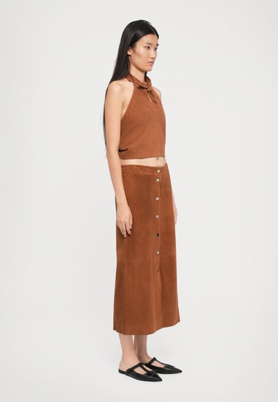 Brun svea crop-top med knytetaske og en matchende lang skjørt med frontknapper og en glatt tekstur. Brukt med sorte spisse leiligheter.