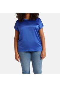 Satin blauwe top met korte mouwen, in een ontspannen pasvorm, gladde textuur en ronde halslijn, gecombineerd met lichtblauwe denim jeans.