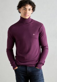 Pull en laine violet avec une texture douce et une coupe ajustée. Petit logo sur la poitrine, associé à un jean foncé.