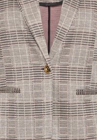 Blazer z tkaniny s tkaným vzorem ve smetanové, černé a hnědé barvě, se jediným hnědým knoflíkem a dvěma předními kapsami.